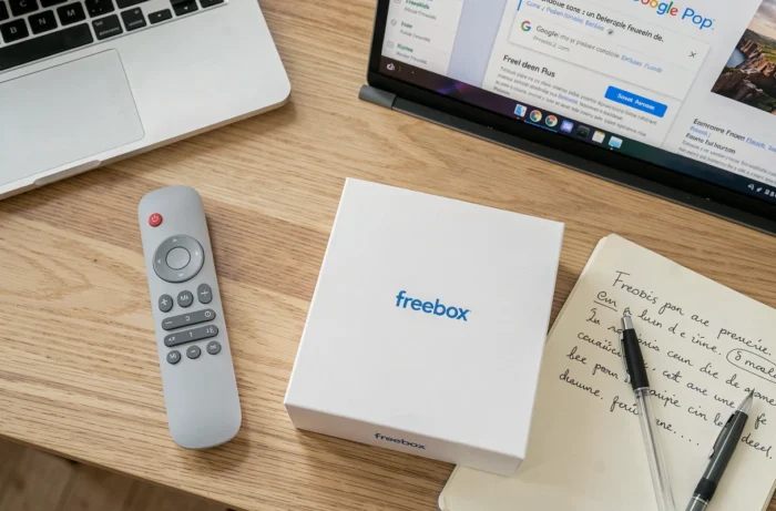 Vue en plongée de la télécommande et du boîtier Freebox Pop sur un bureau avec un guide des paramètres Google ouvert sur un ordinateur portable