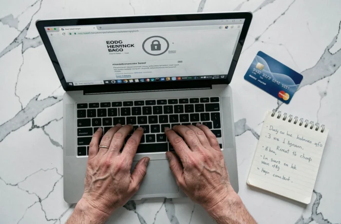 Vue aérienne de mains tapant sur un ordinateur portable avec une carte bancaire sur un bureau en marbre, illustrant la gestion sécurisée des données financières en ligne